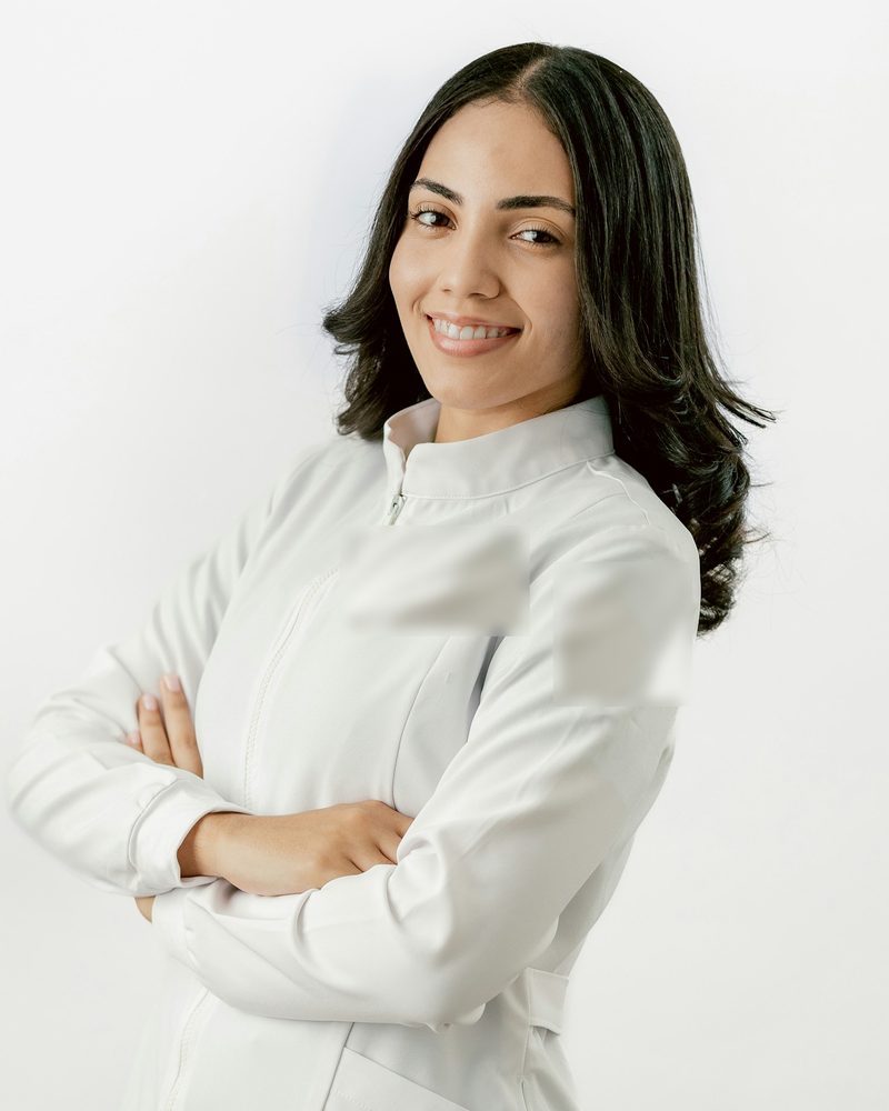 Portrait von Dr. med. Lena Hartmann mit dunklen, schulterlangen Haaren im weißen Kittel, lächelnd, vor hellem Hintergrund